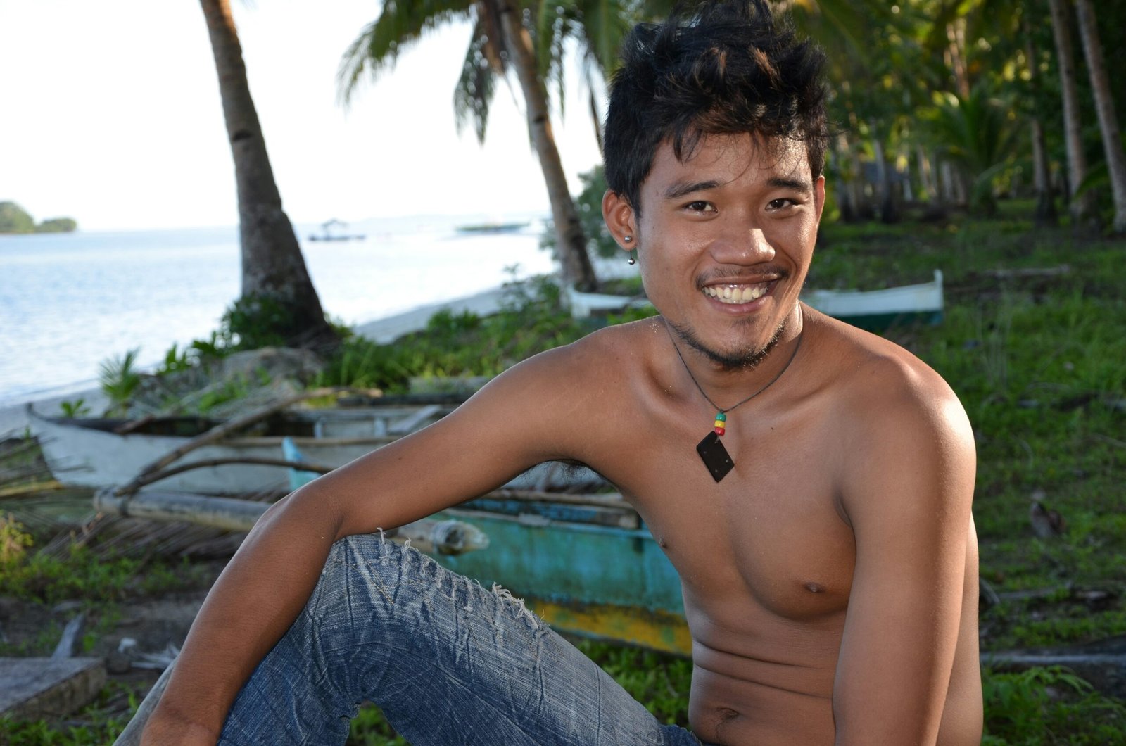Young Filipino community leader Miguel Santos sitting by coastal area with traditional bancas, representing CJF Philippines Youth for Resilience program